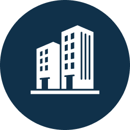 White icon of two multi-story buildings on a dark blue circular background.